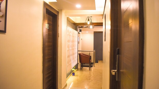 A hallway with a wooden door on the right, a chair in the center, and a small plant on the floor. - Hotel Mumbai International (Mumbai)