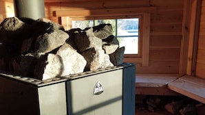 A wood-burning stove with a visible fire, stacked firewood, and a window in the background. - Blankaholms Bad och Naturcamping (Hjorted)