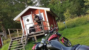 A red wooden structure with a door and a small porch. - Blankaholms Bad och Naturcamping (Hjorted)