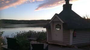 A wooden cabin with a thatched roof by a lake, a dock, and a bench. - Blankaholms Bad och Naturcamping (Hjorted)