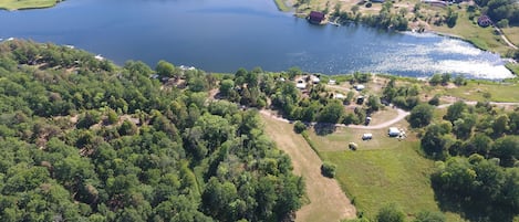 An aerial view of a lakeside property with a mix of forested areas and open fields, a small dock, and a few scattered buildings.