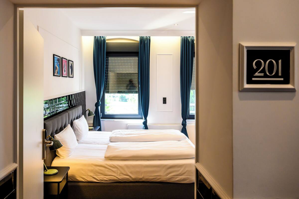 A hotel room with a bed, a nightstand, a lamp, and a window with curtains.