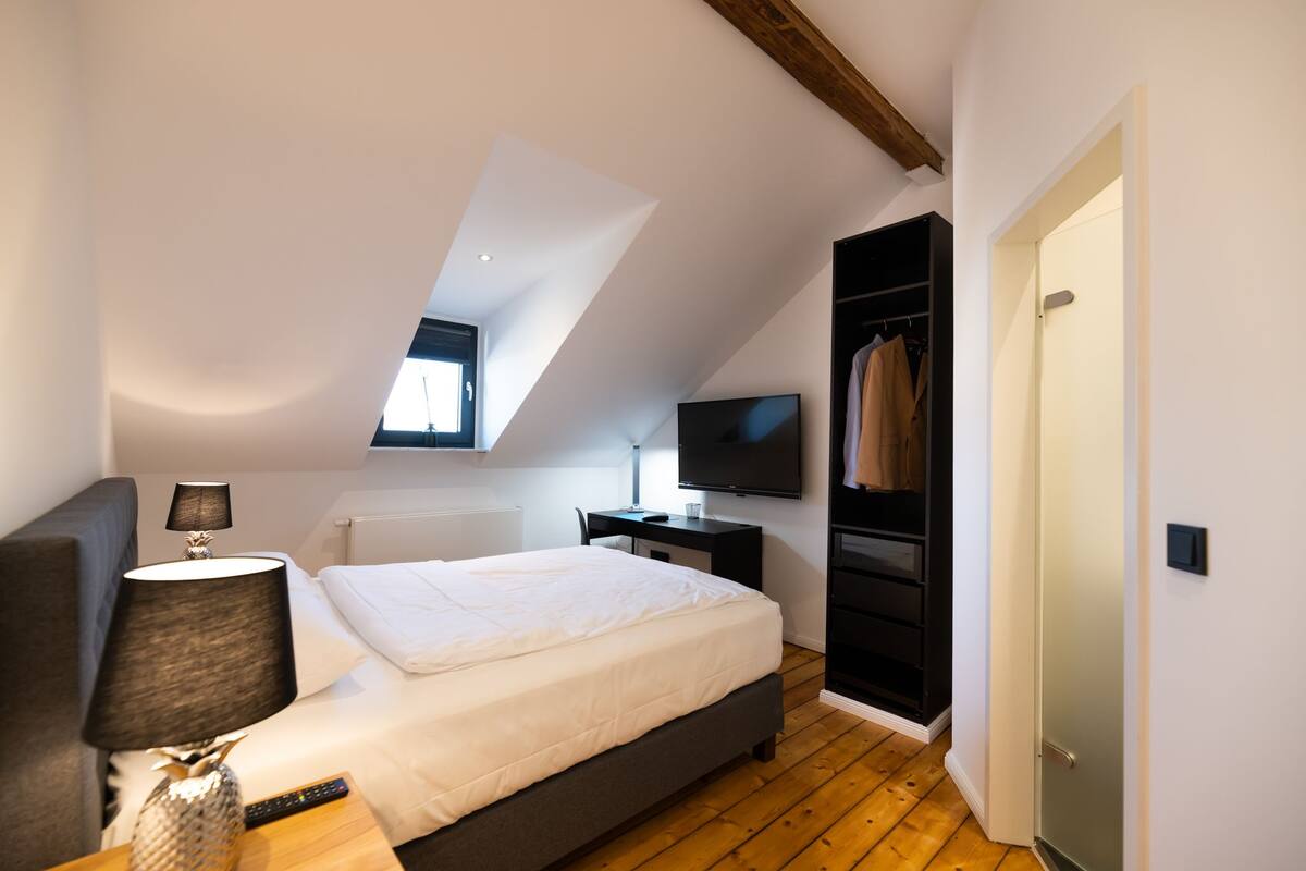 A bedroom with a bed, a desk, a TV, and a wardrobe.