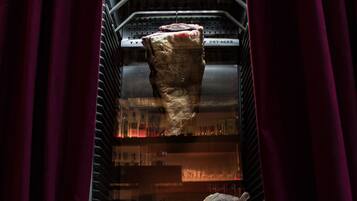 A dry aging display case with a large piece of meat and two smaller ones, illuminated by internal lighting.