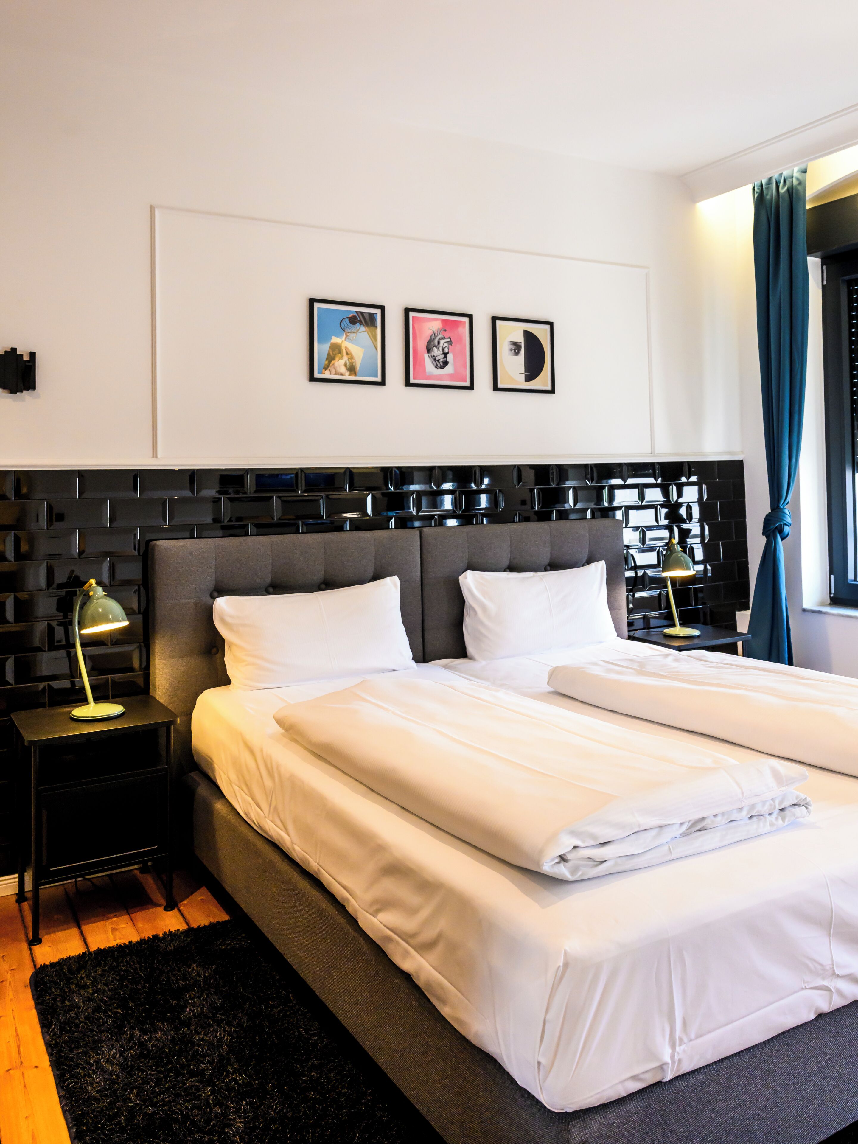 Une chambre d’hôtel moderne avec un grand lit, une table de chevet, une lampe et des œuvres d’art accrochées au mur.
