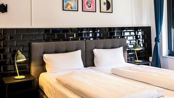 A modern hotel room with a large bed, a nightstand, a lamp, and artwork on the wall.