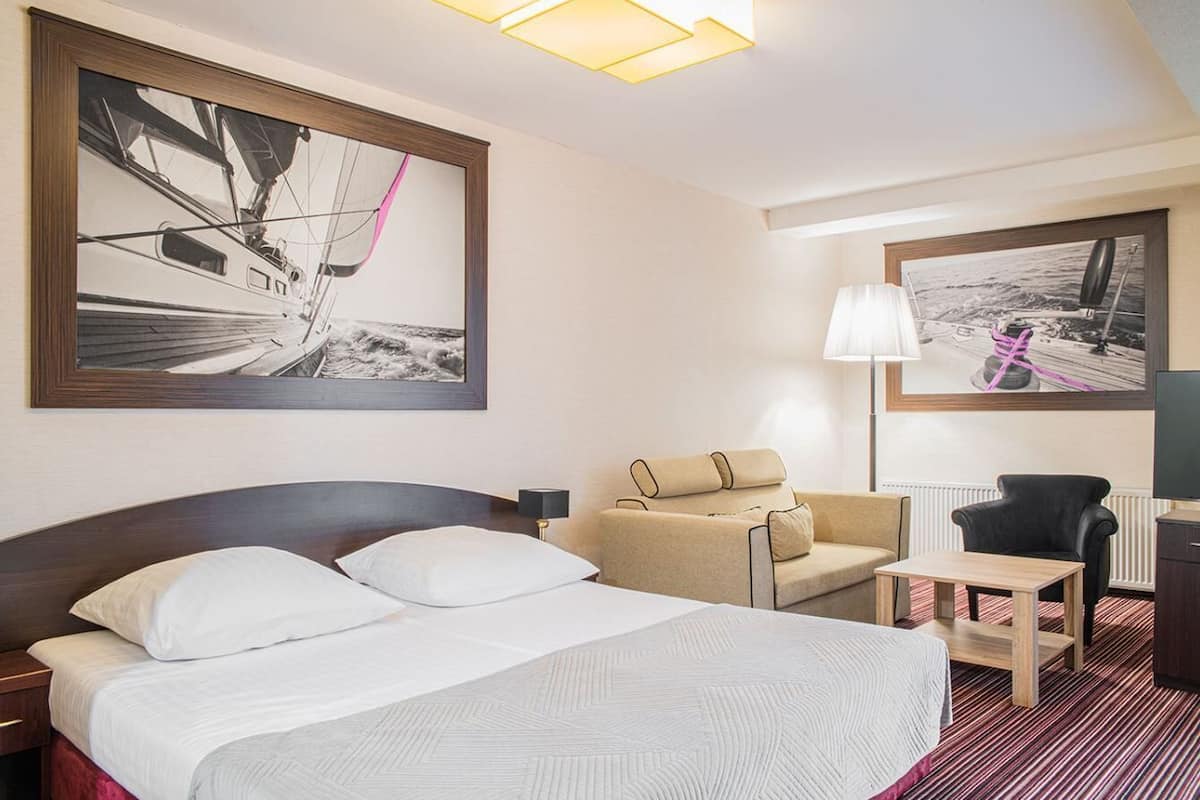A hotel room with a large bed, a sofa, a desk, and two framed pictures on the walls.