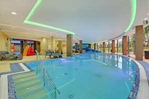 Una piscina interior con techo curvo, agua cristalina y un tobogán.