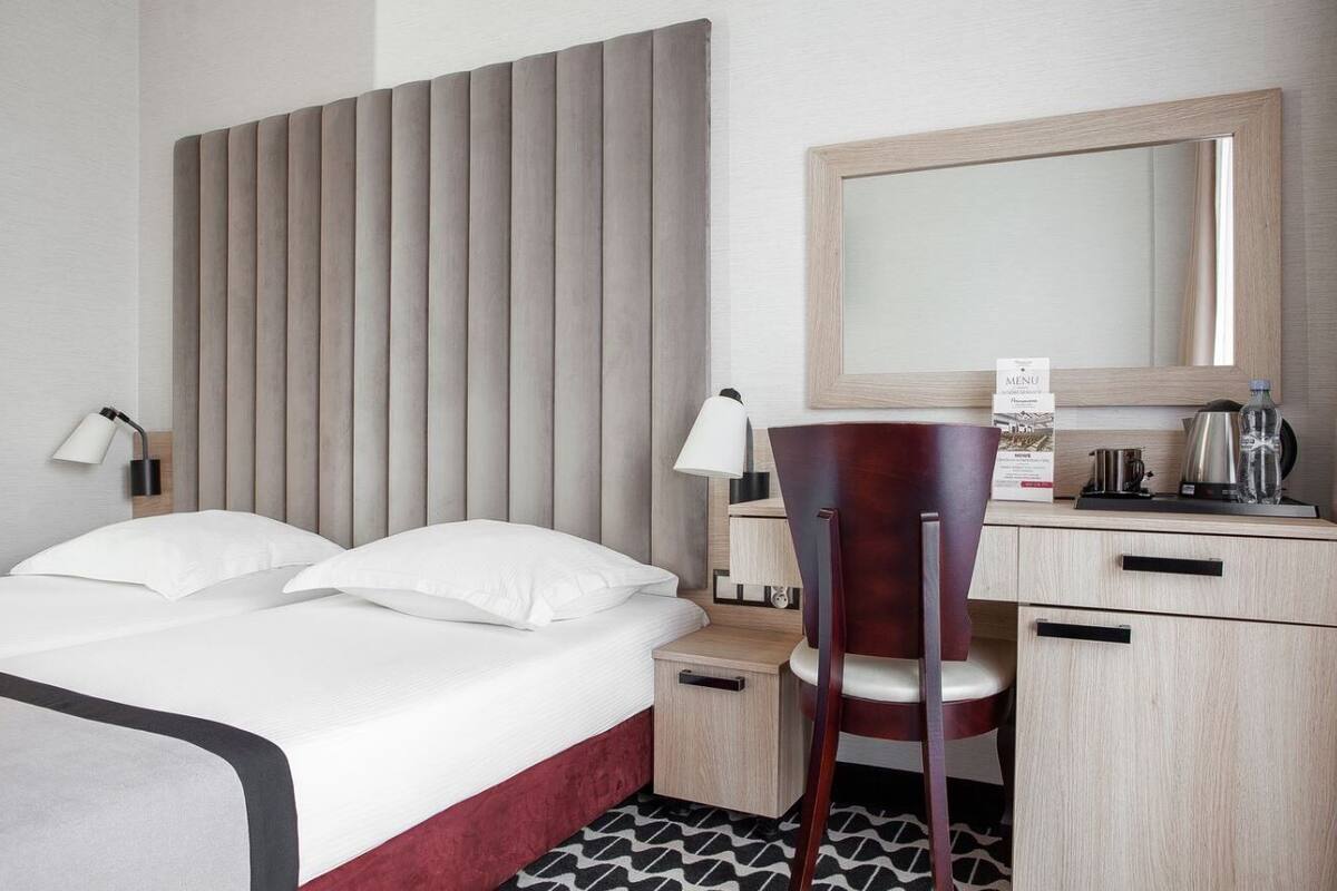 A hotel room with a bed, bedside table, chair, desk, and a mirror.