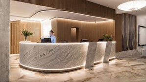 A reception desk with a marble finish, wooden paneling on the walls, and a modern light fixture. - Primavera Jastrzębia Góra (Wladyslawowo)