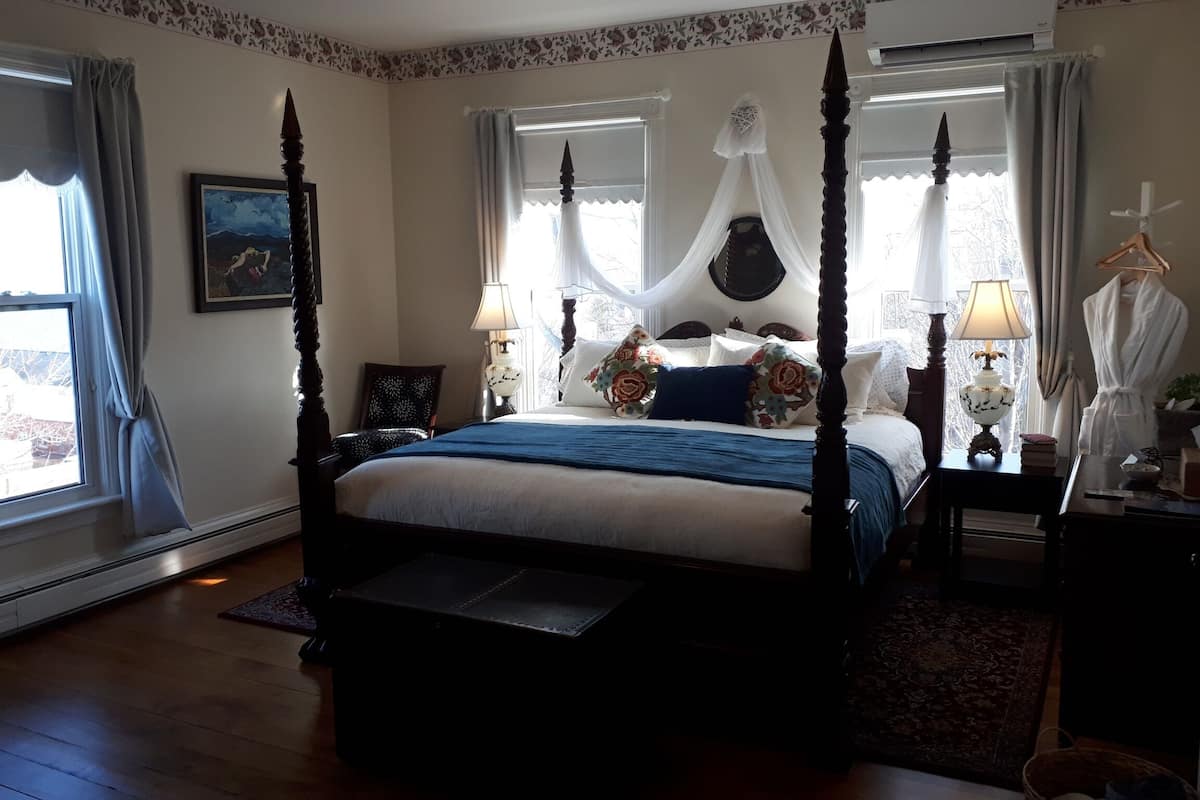 A four-poster canopy bed with a blue bedspread, floral pillows, and a bedside table with a lamp.