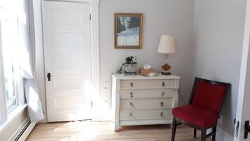 A room with a white dresser, a red chair, a lamp, and a painting on the wall.