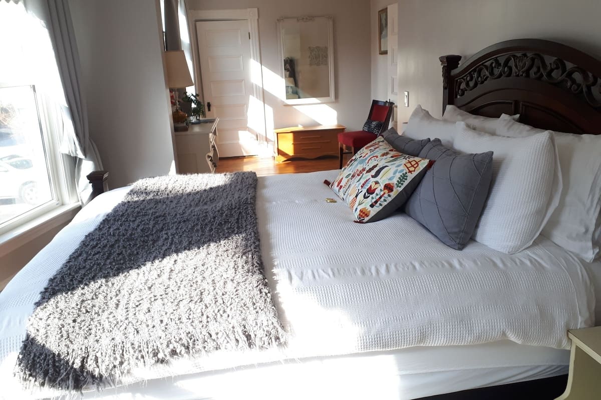 A neatly made bed with a patterned pillow, a gray throw blanket, and a wooden headboard.