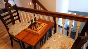 A wooden chessboard on a chair with a floral cushion, positioned near a staircase with white balusters. - Hillside Landing B&B (Digby)