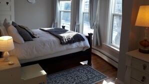 A bedroom with a bed, bedside tables, a clock, and windows with curtains. - Hillside Landing B&B (Digby)