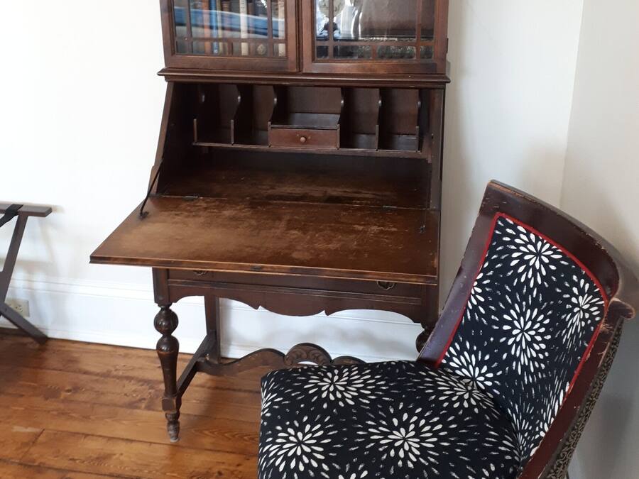 Un mueble de madera con puertas de cristal, una mesa de madera y una silla con estampado.