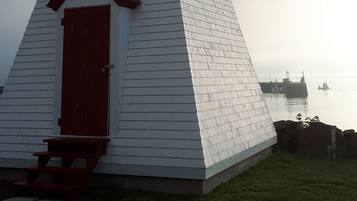 Un phare à l’extérieur blanc et à la porte rouge, situé sur une zone herbeuse près d’une étendue d’eau.