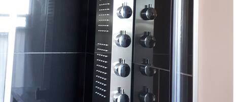 A modern bathroom with black tiles, a glass shower enclosure, and a decorative brick pattern on the wall.