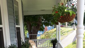 A covered porch with wooden Adirondack chairs, a white railing, and potted plants. - Hillside Landing B&B (Digby)