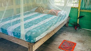 Ein Bett mit Moskitonetz, Holzrahmen und einem gemusterten Überwurf.