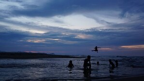 Eine Strandansicht mit Personen im Wasser und einem Sonnenuntergang im Hintergrund.
