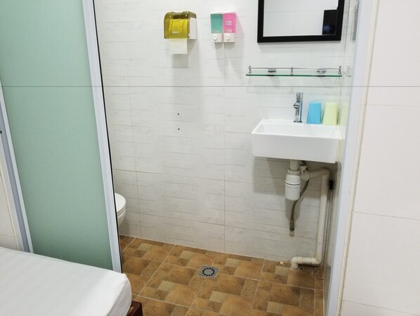 Une salle de bain avec des murs carrelés de carreaux blancs, un lavabo équipé de distributeurs de savon et des toilettes.
