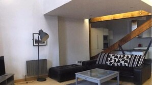 A modern living room with a sofa, a coffee table, a floor lamp, and a staircase. - Luxurious City Centre Penthouse (Newcastle-upon-Tyne)