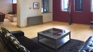 A living room with a black sofa, a glass coffee table, and a red accent wall. - Luxurious City Centre Penthouse (Newcastle-upon-Tyne)