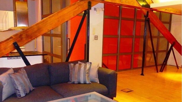 A modern living room with a glass-top coffee table, a gray sofa with cushions, and a wooden staircase. - Luxurious City Centre Penthouse (Newcastle-upon-Tyne)