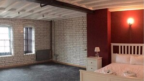 A bedroom with a white bed, a nightstand, a window, and a brick wall. - Luxurious City Centre Penthouse (Newcastle-upon-Tyne)