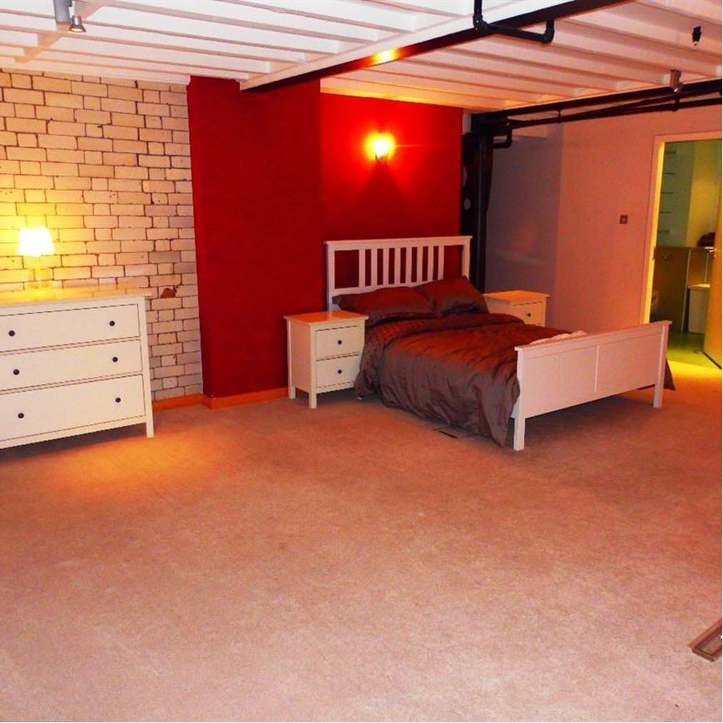 A bedroom with a bed, nightstands, a dresser, and a red accent wall.