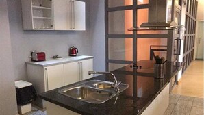 A modern kitchen with a black countertop, stainless steel sink, white cabinets, and a window with a view. - Luxurious City Centre Penthouse (Newcastle-upon-Tyne)