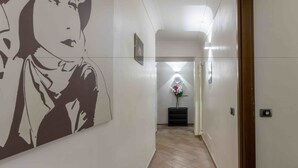 Un pasillo con un gran mural en la pared, una escalera y una pequeña mesa con un florero.