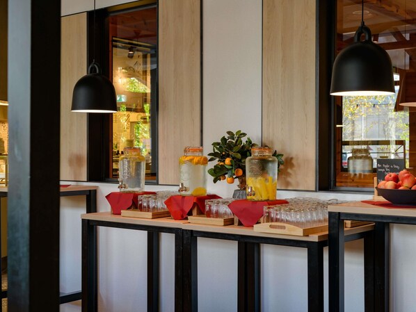 A bar area with a wooden counter, glass jars with beverages, a bowl of fruit, and hanging pendant lights. - Mercure Zürich City (Zürich)