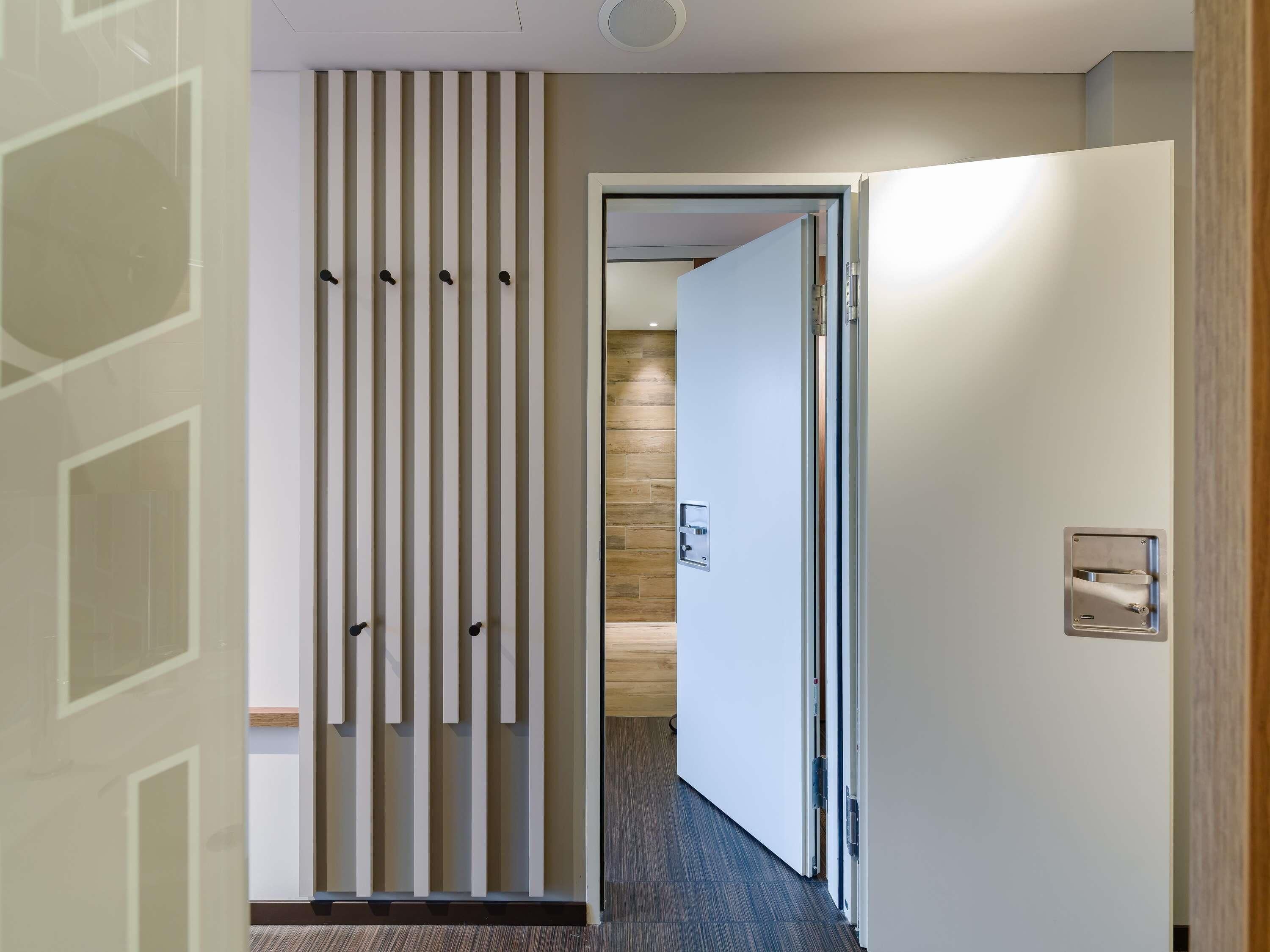Um corredor com design moderno, apresentando um painel vertical com ganchos, uma porta com puxador e um interruptor de luz na parede.
