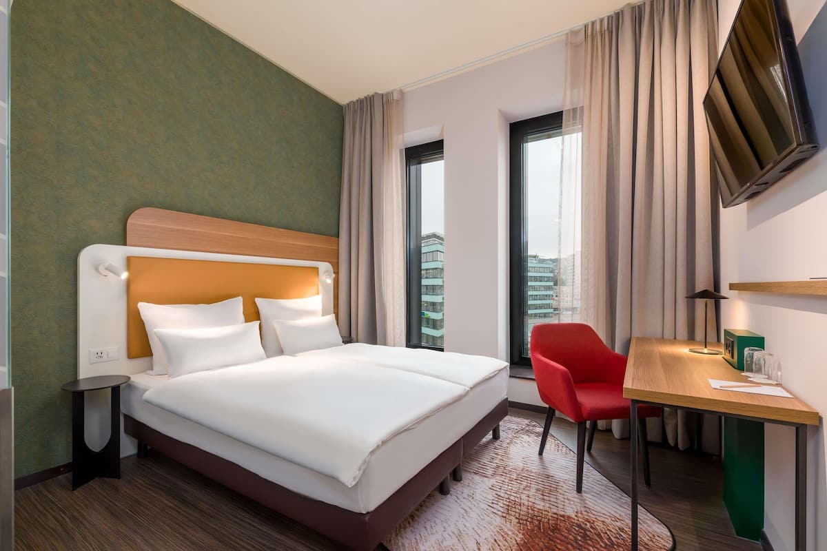 Une chambre d’hôtel avec un grand lit, un bureau, une chaise et un téléviseur fixé au mur.