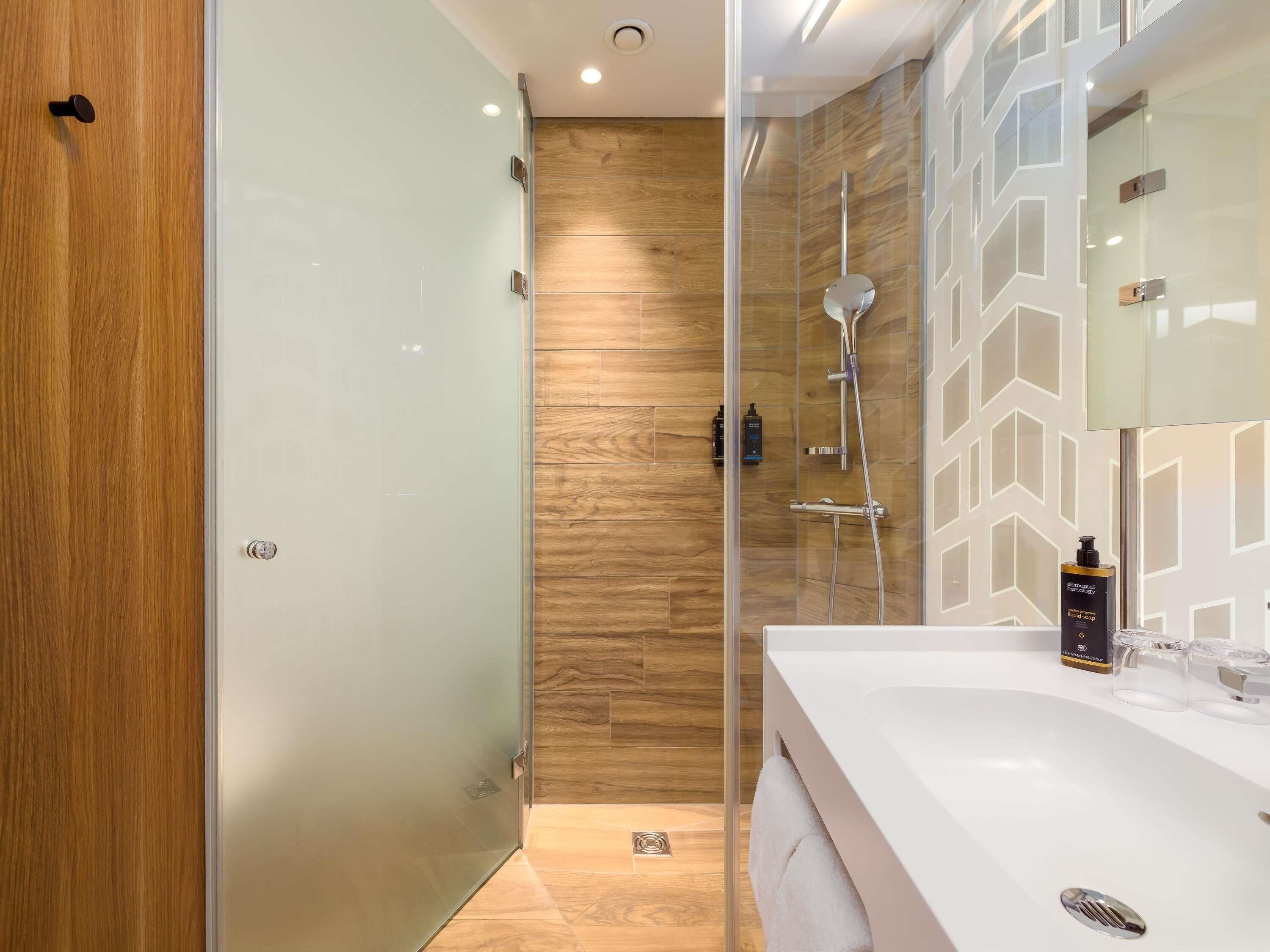 A modern bathroom with a glass shower enclosure, a wooden wall, and a white sink with a mirror.