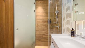 A modern bathroom with a glass shower enclosure, a wooden wall, and a white sink with a mirror.