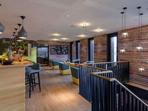 A modern interior with a wooden floor, seating areas, a reception desk with fruit, and a chalkboard menu.