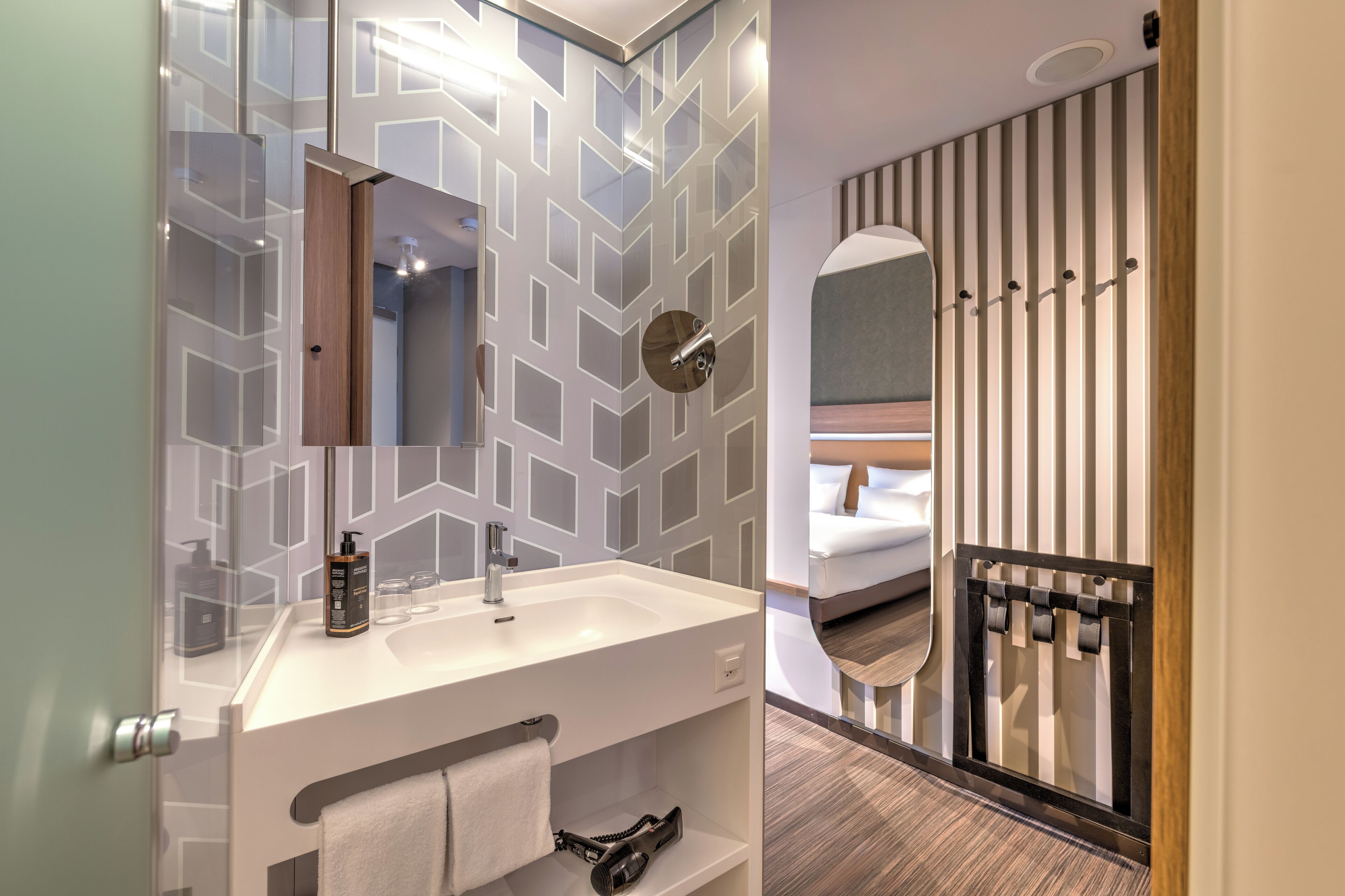 Un baño moderno con un revestimiento de pared de diseño geométrico, un lavabo blanco, un espejo y un perchero.