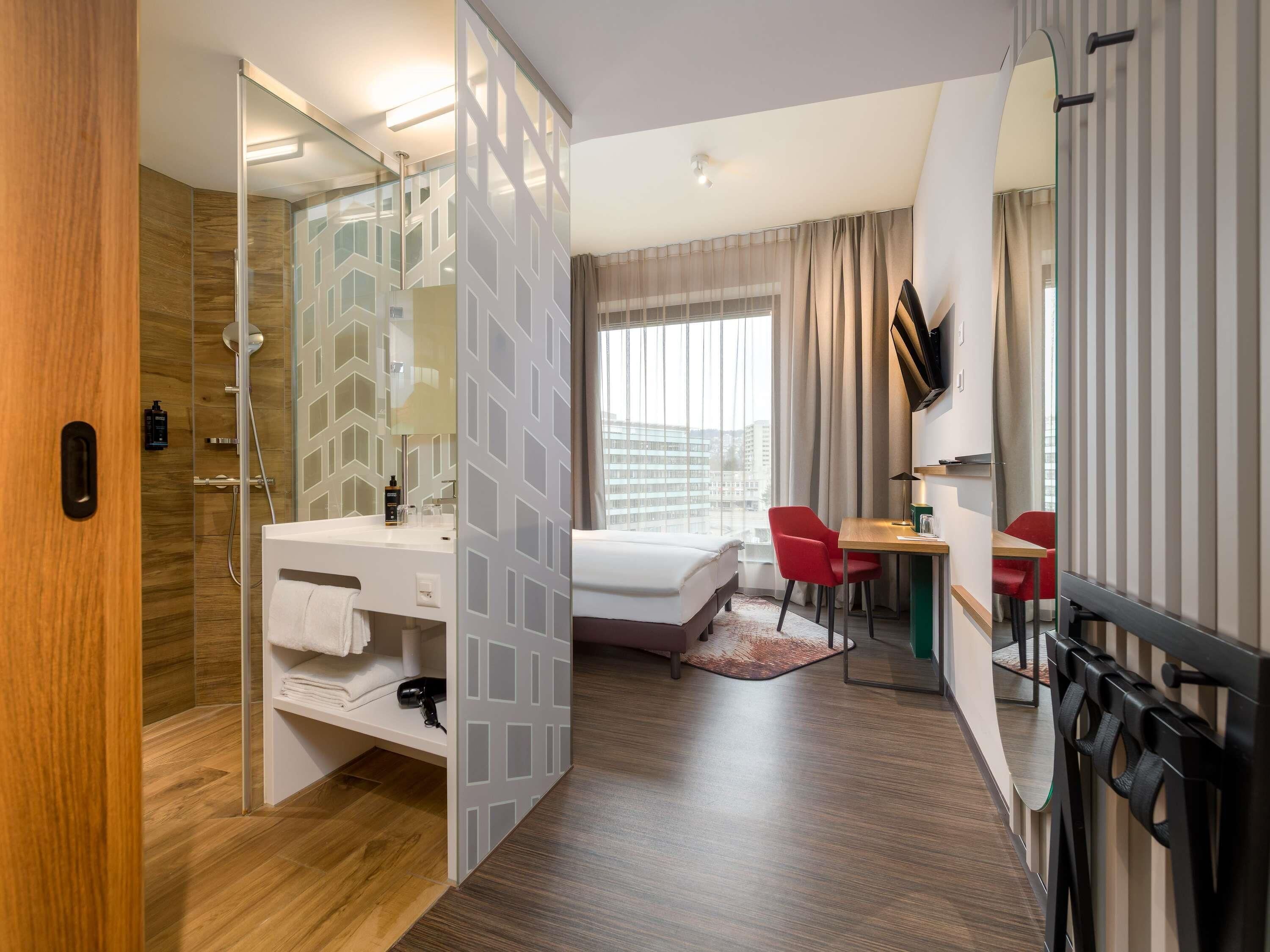 A modern hotel room with a shower, a bed, a desk, and a chair.
