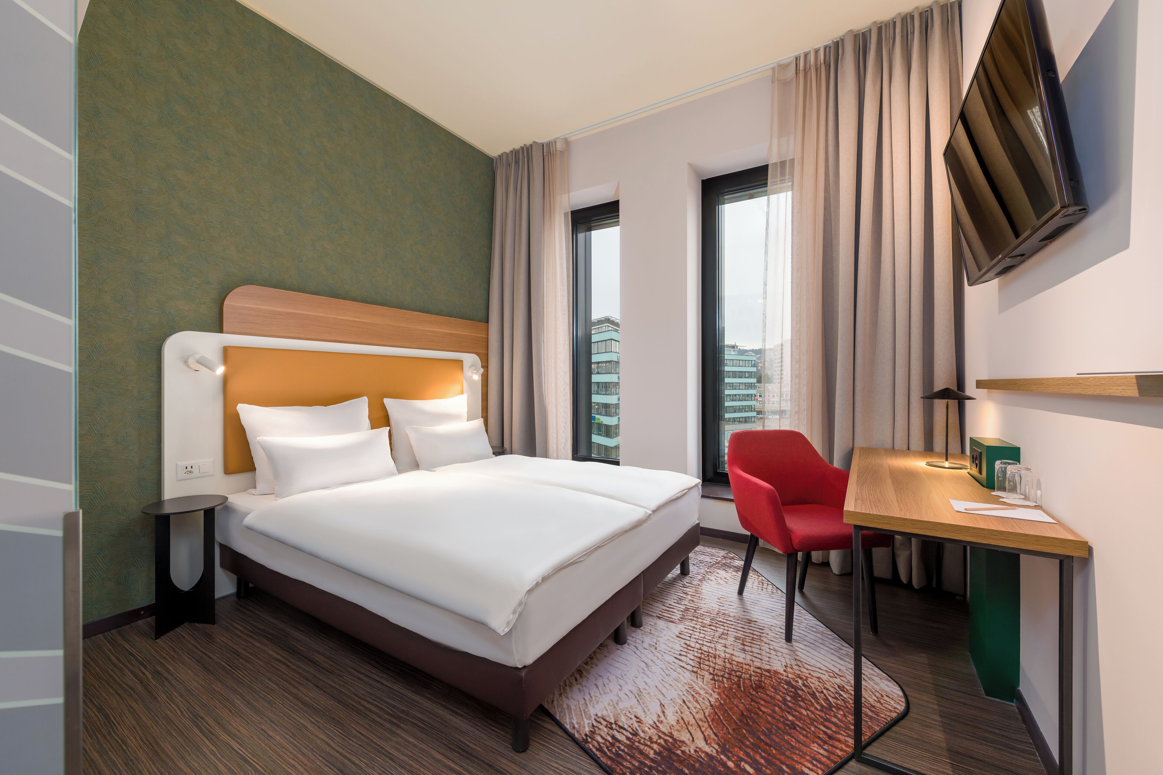 Quarto de hotel com cama, escrivaninha, cadeira, televisão e vista para a cidade.