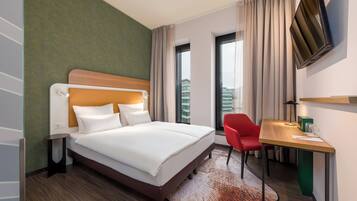 Quarto de hotel com cama, escrivaninha, cadeira, televisão e vista para a cidade.
