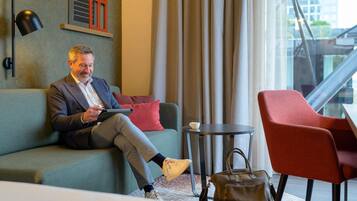 A man sitting on a sofa in a modern hotel room with a view of a building outside.