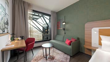 Ein Hotelzimmer mit einem Holztisch, einem roten Sessel, einem grünen Sofa und einem runden Tisch.