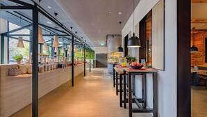 A modern hotel corridor with a long reception desk, pendant lighting, and a view of the kitchen area.