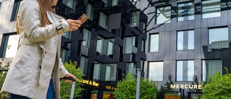 A person with a suitcase standing in front of a modern building with a glass facade and a sign for 'MERCURE'.
