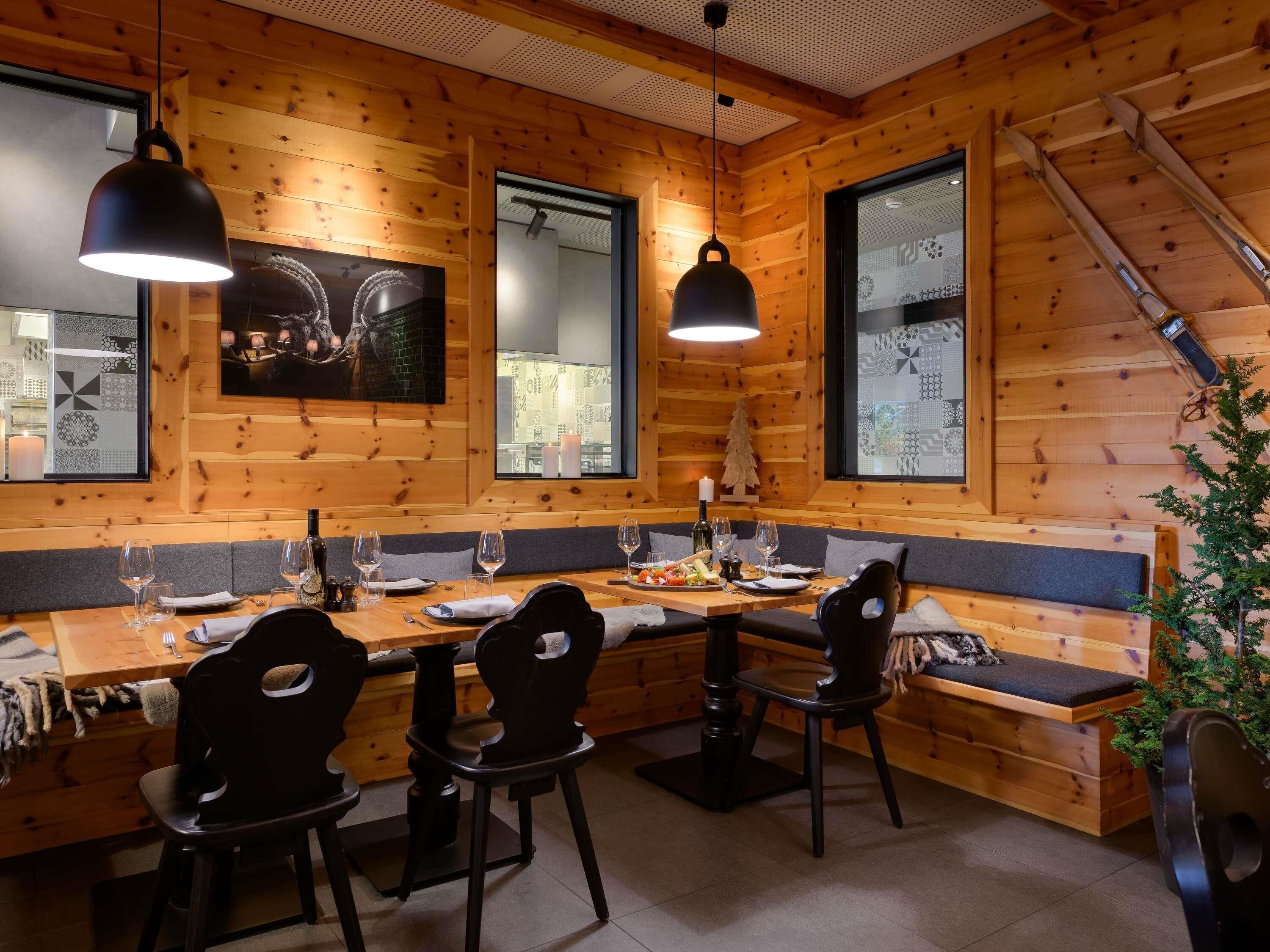 A wooden cabin interior with a dining table, chairs, pendant lights, and a staircase.