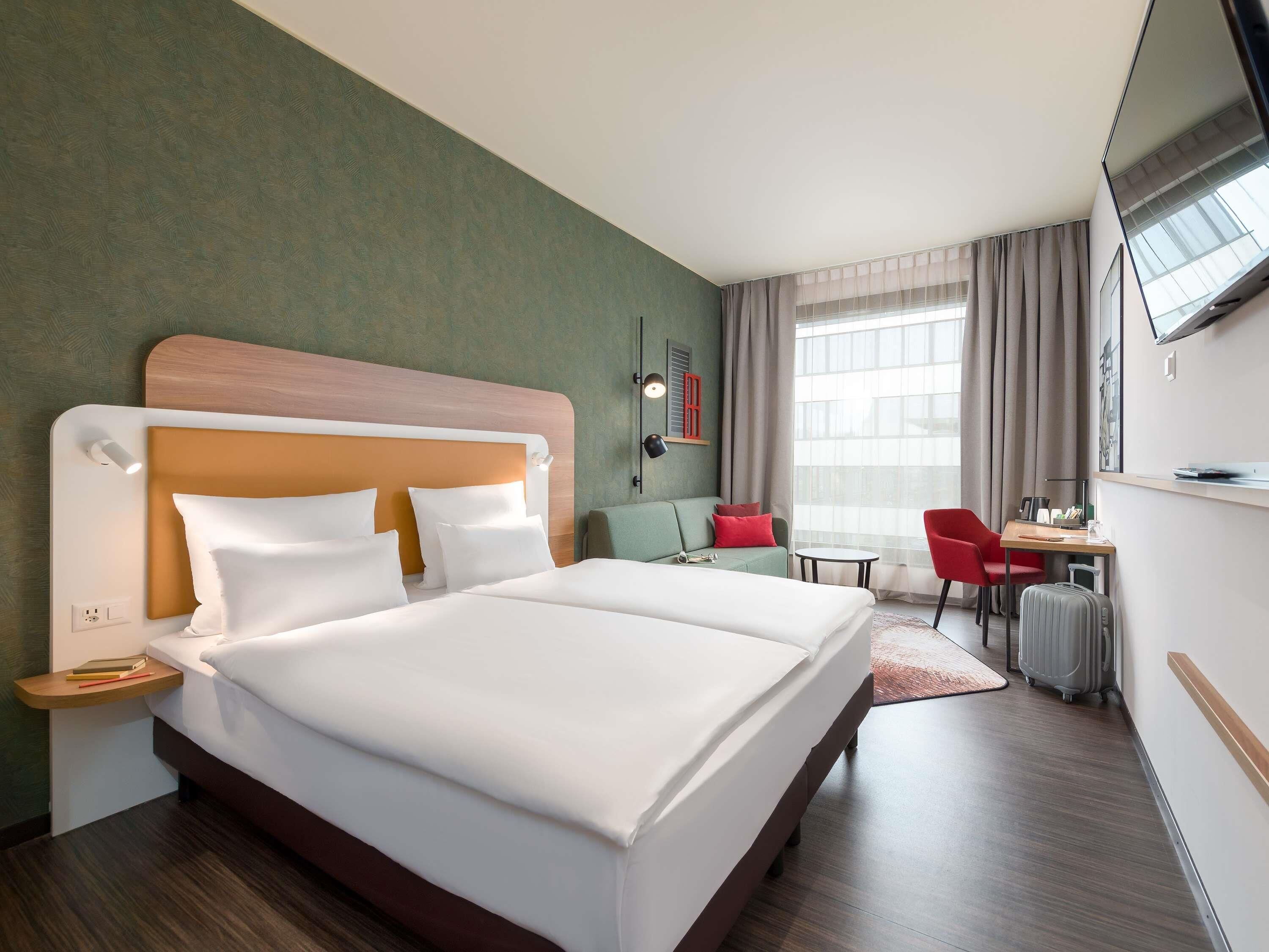 A hotel room with a large bed, a desk, a chair, and a TV.