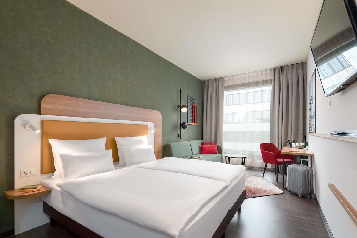 A hotel room with a large bed, a desk, a chair, and a TV.